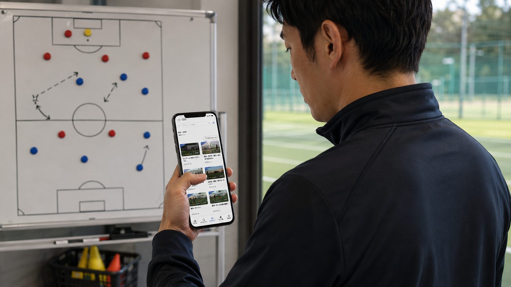 作戦ボードの前でスマホの練習メニュー一覧を見る指導者